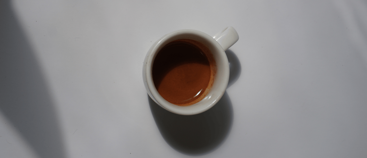 Overhead view of a single espresso shot in a white cup on a light background, showing rich crema.