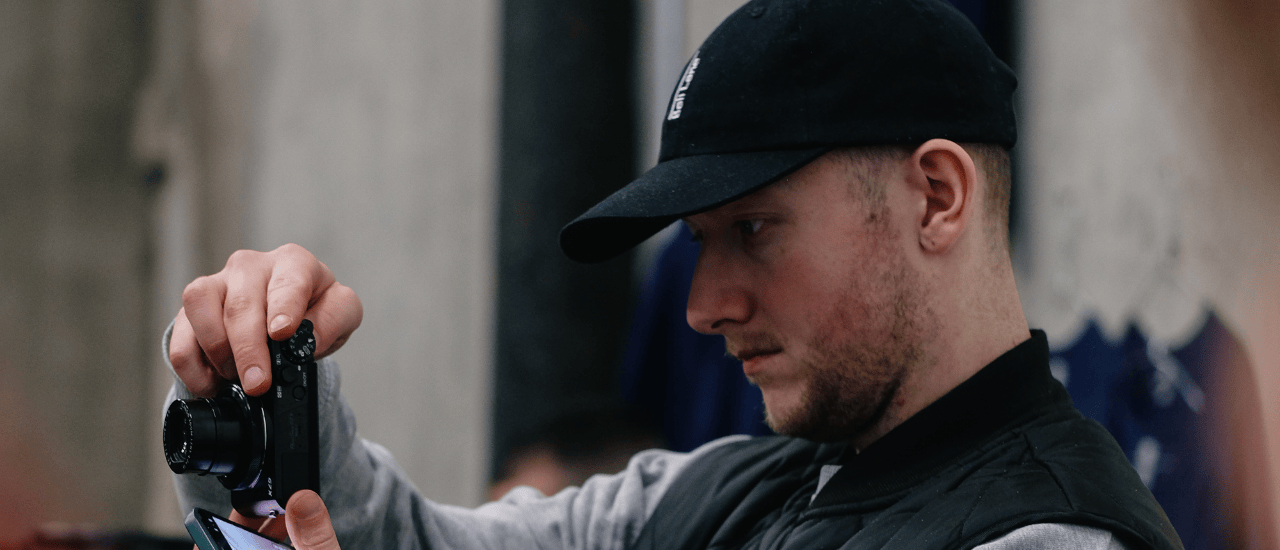 Paul Flaherty from Bell Lane Coffee Roasters focused on capturing a photo, holding a camera and smartphone. Wearing a black cap and jacket, with a blurred background at Dublin Coffee Festival 2024.