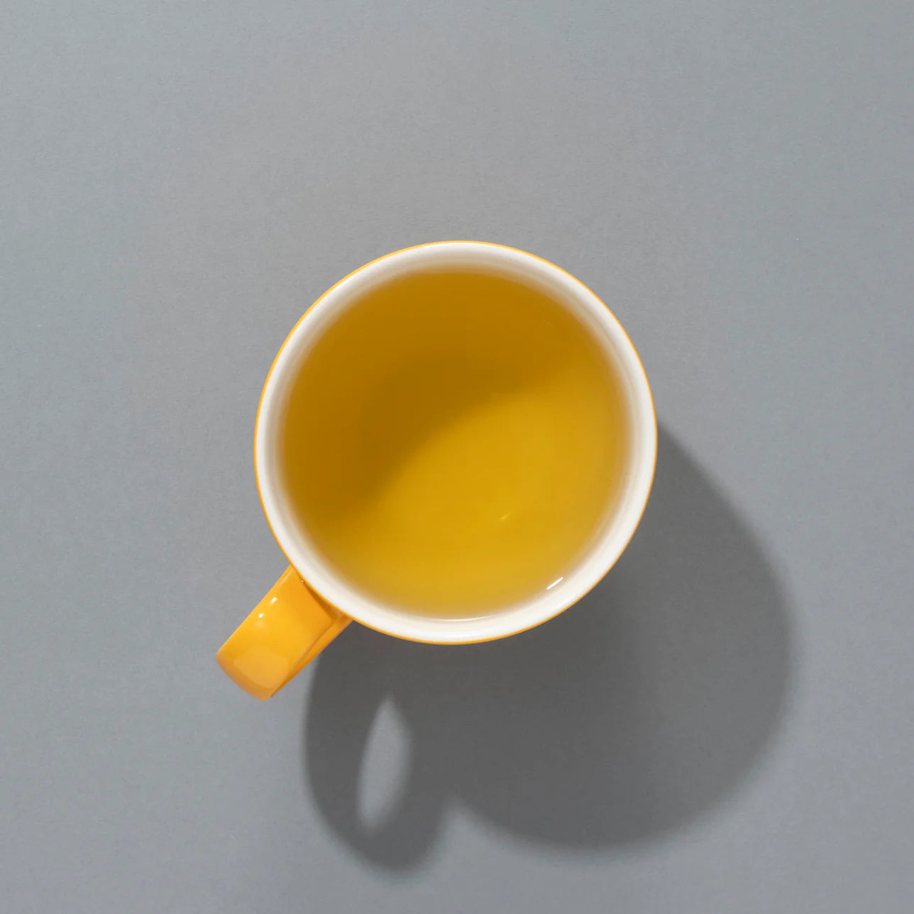 A cup of brewed Suki Tea Makers Lemongrass and Ginger herbal infusion in a yellow mug, viewed from above on a grey background.