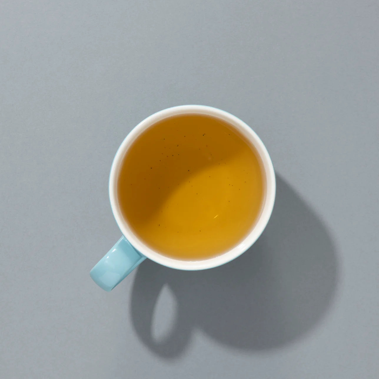 A cup of brewed peppermint tea in a light blue mug, viewed from above against a grey background.