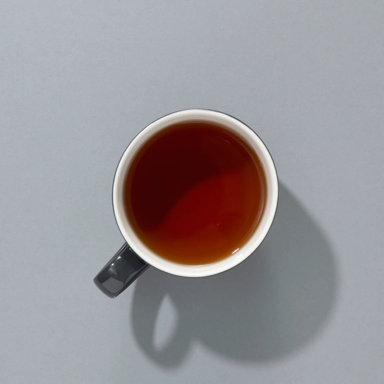 White mug with black handle filled with tea on a gray background.