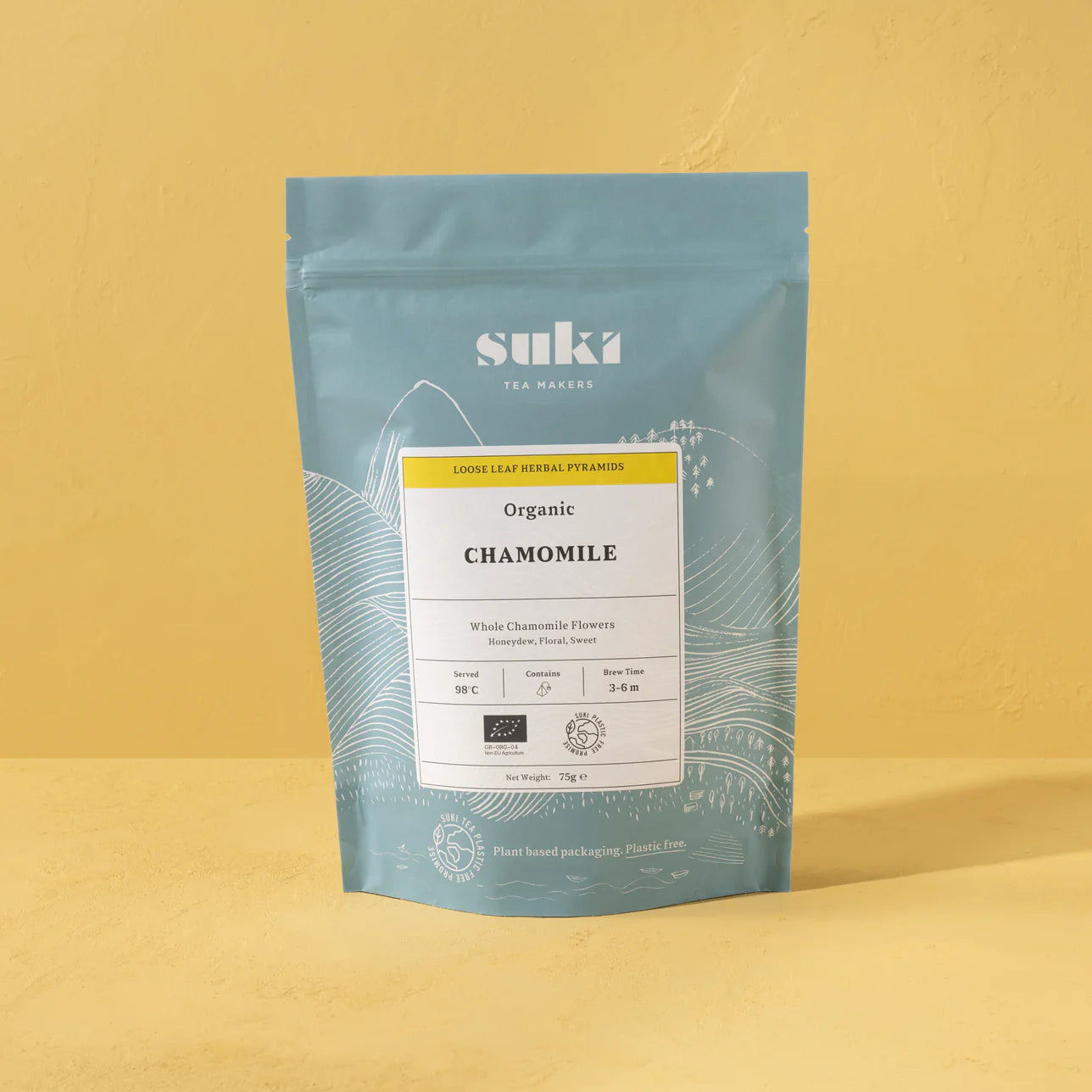 Suki Tea Makers Organic Chamomile loose leaf herbal tea in blue and yellow plant-based packaging, standing against a soft yellow background.