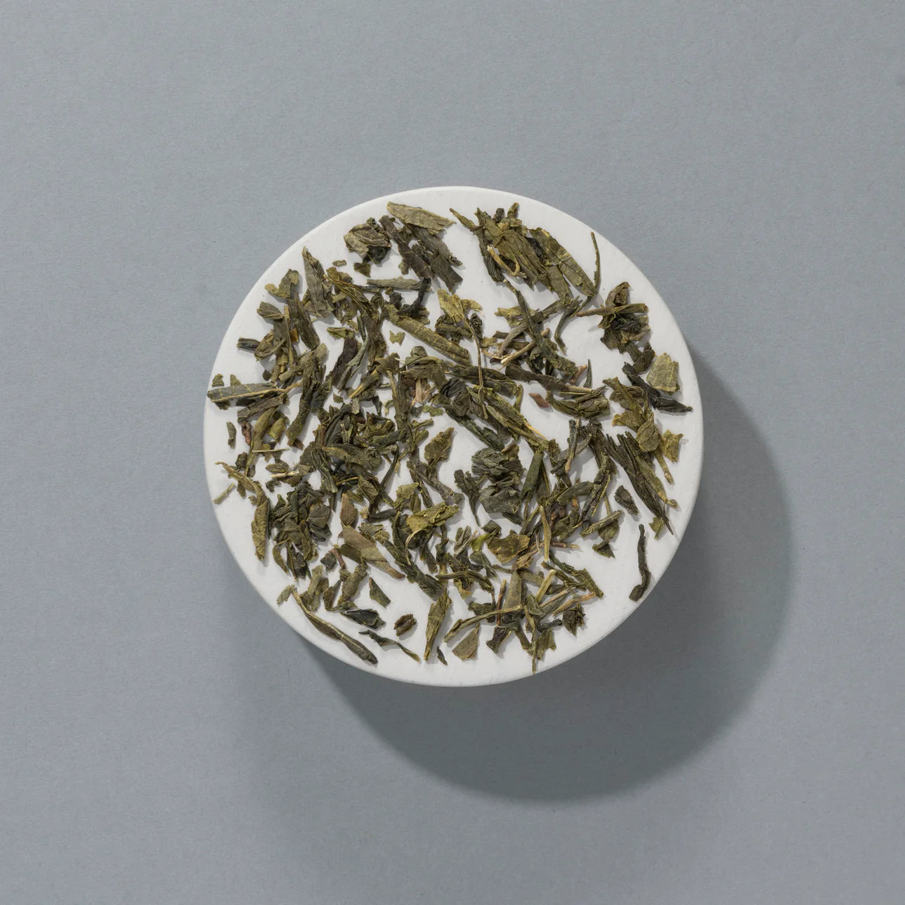 Loose Sencha green tea leaves displayed on a white ceramic plate.