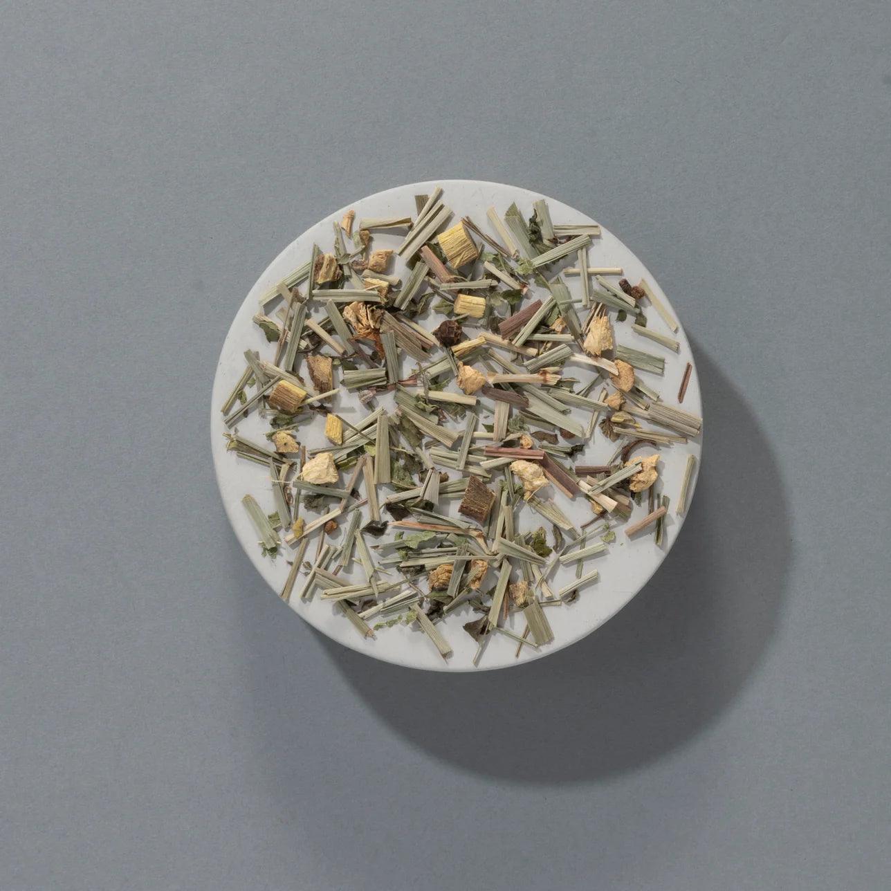 Loose leaf blend of Suki Tea Makers Lemongrass and Ginger, displayed on a round white dish against a grey background.