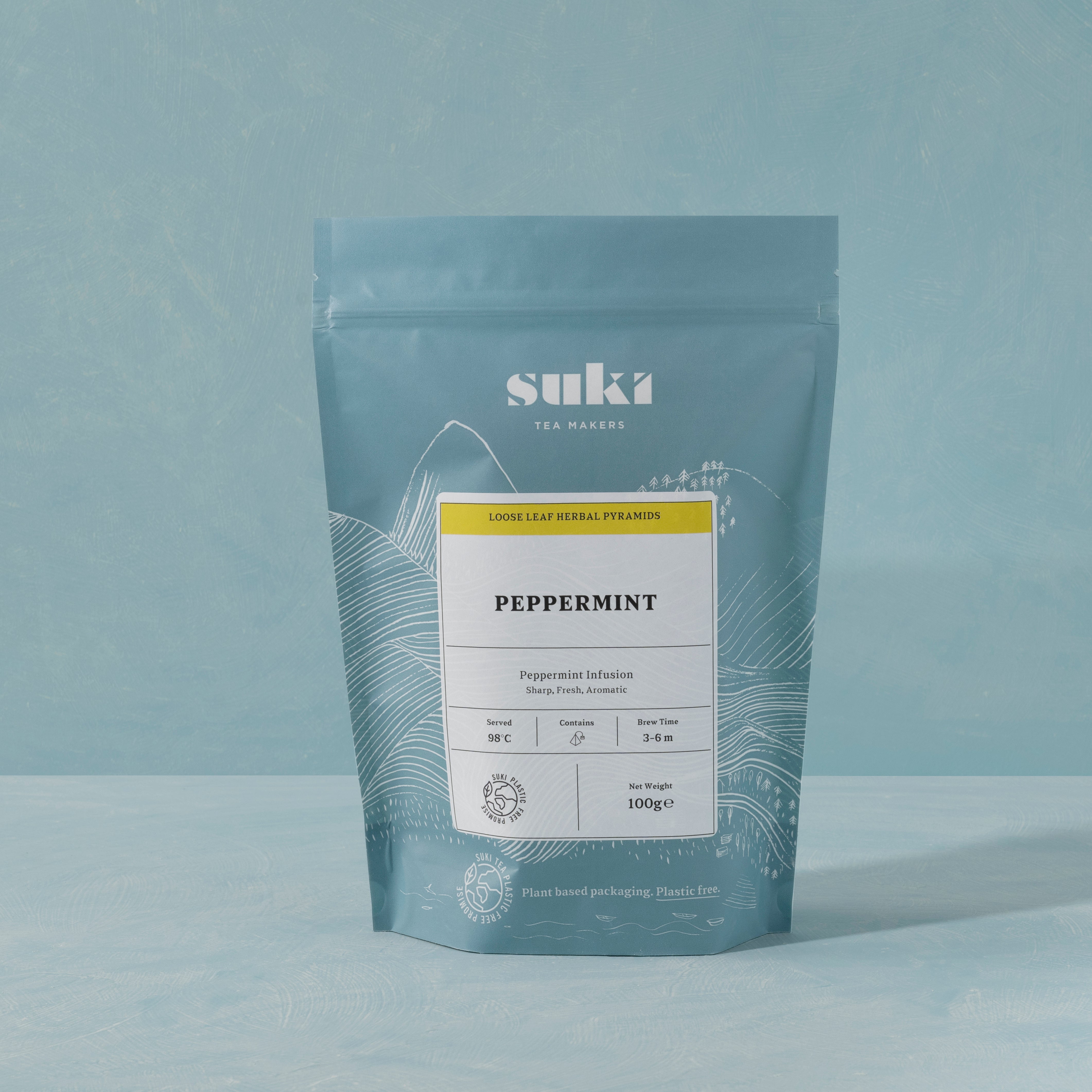Suki Tea Makers Peppermint loose leaf herbal tea in blue and yellow plant-based packaging, set against a soft teal background.