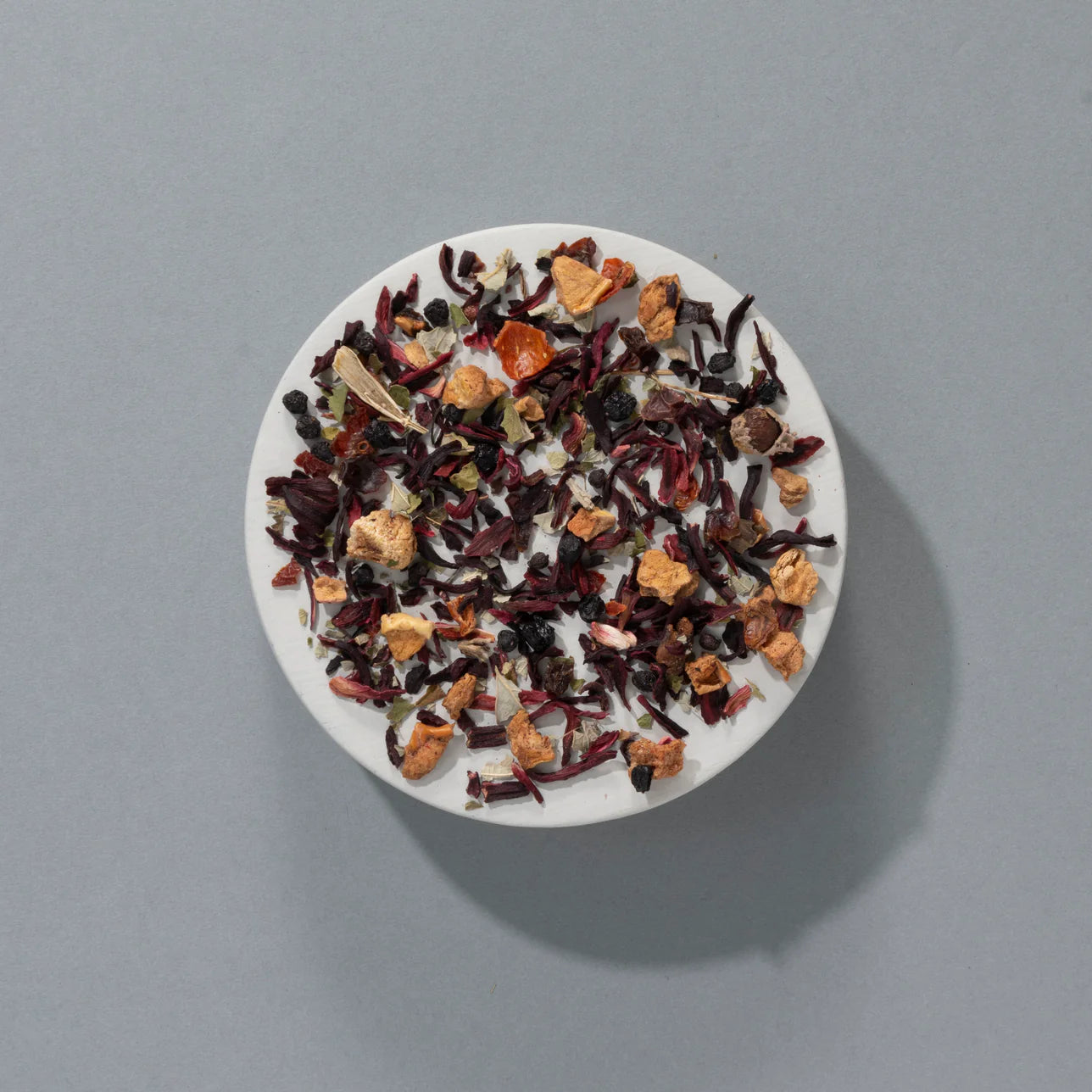 Loose Red Berry infusion with dried hibiscus, fruit pieces, and berry chunks on a ceramic plate.